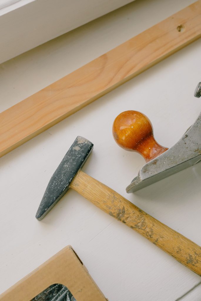 From above of hammer near jointer with wooden knob and plank on white surface at home